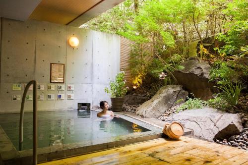 Una donna è seduta in una piscina in un giardino di Izumigo AMBIENT Yatsugatake Cottage a Hokuto