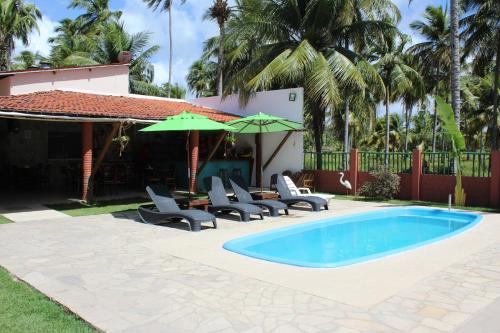 a pool with chairs and umbrellas next to a house at Pousada Recanto dos Milagres in São Miguel dos Milagres