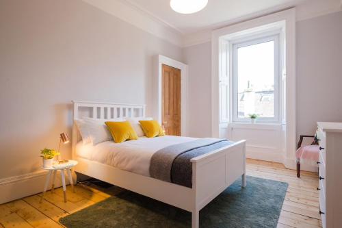 a bedroom with a bed with yellow pillows and a window at Historic Edinburgh 1890s Home Turned Relaxing Retreat in Edinburgh