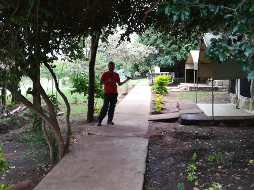 a man standing on a sidewalk next to trees at Oldarpoi Wageni Camps in Keekorok