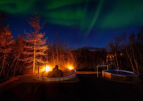 two people sitting in a tub under the northern lights at Hotel Kjarnalundur- Aurora Dream - Lodges and Rooms in Akureyri