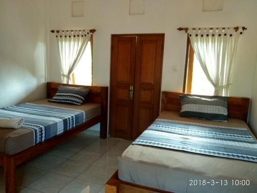 two beds in a room with two windows at Medewi Beach Inn in Pulukan
