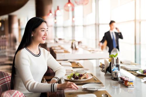 Pullman Nanjing Lukou Airport في نانجينغ: امرأة تجلس على طاولة مع طبق من الطعام