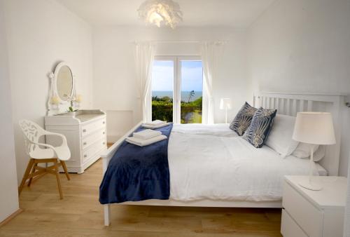 ein weißes Schlafzimmer mit einem großen Bett und einem Fenster in der Unterkunft E&M Beach House Aldeamento do Levante II in Lagoa