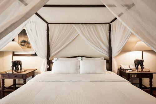 a bedroom with a bed with white bedding and two night stands at Safari Park Hotel in Nairobi