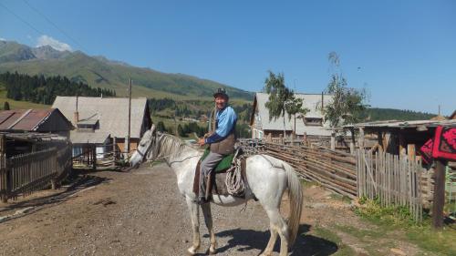a man riding a white horse in a village at Syimyk Guest House in Dzhergalan