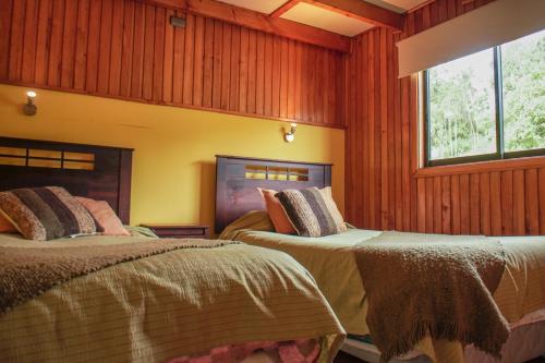 Duas camas num quarto com paredes com painéis de madeira em Cabañas Palafitos Los Pescadores em Castro