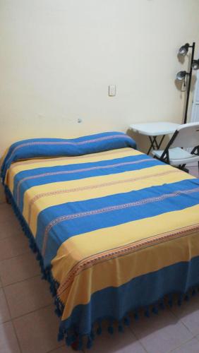 una cama con sábanas azules y amarillas junto a una mesa en Amplias Y Confortables Habitaciones Amuebladas, en San Juan Bautista Tuxtepec
