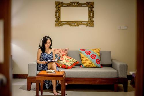 a woman sitting on a couch reading a book at Rama Residence Petitenget in Seminyak