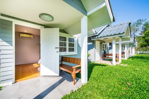 a house with a porch with a bench on a lawn at Ivy Cottage by Qiu in Sara Buri