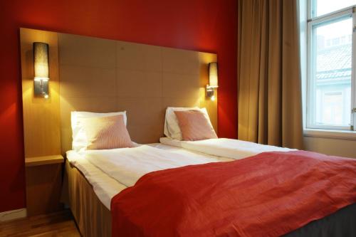 a bedroom with a large bed with a red wall at City Living Schøller Hotel in Trondheim