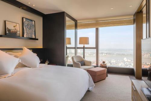 a bedroom with a large white bed and large windows at Rosewood Phnom Penh in Phnom Penh