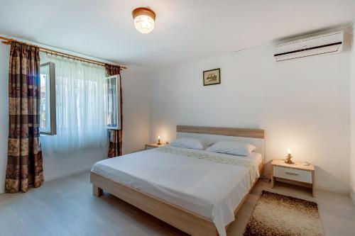 a white bedroom with a bed and a window at Apartments Ivna in Veli Lošinj