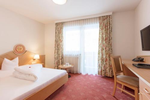 a hotel room with a bed and a desk and a window at Hotel Andreas Hofer in Sankt Leonhard im Pitztal