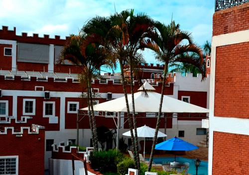 twee palmbomen en parasols voor een gebouw bij Medieval Hotel in Três Corações