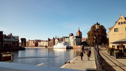 two people walking down a sidewalk next to a river at Apartament MARIA in Gdańsk