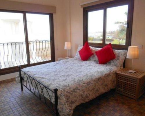 sypialnia z łóżkiem z czerwonymi poduszkami i 2 oknami w obiekcie “villa with a pool in a fantastic location” Protaras Villa 49 w mieście Protaras