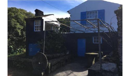 uma pequena casa azul com um edifício ao fundo em Adega guest house em Horta