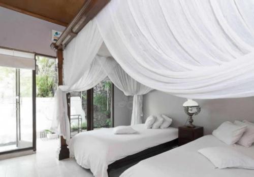 two beds in a bedroom with white curtains at Baliku Dive Resort in Amed