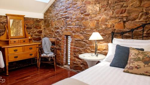 a bedroom with a stone wall with a bed and a desk at Byronsvale Vineyard and Accommodation in Bendigo