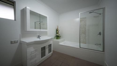 La salle de bains blanche est pourvue d'un lavabo et d'une douche. dans l'établissement Watersons at Airlie Central Apartments, à Airlie Beach