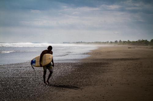 a man walking on the beach with a surfboard at Miguel Surf Camp in Quepos