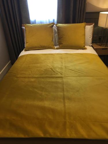 a bed with yellow sheets and pillows in a room at The Tower Arms Hotel in Iver