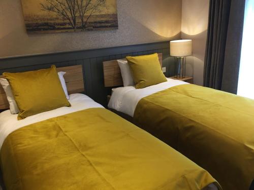 two beds in a hotel room with yellow sheets at The Tower Arms Hotel in Iver