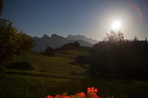 a sun setting over a green field with mountains at Hotel Arvenbüel in Amden