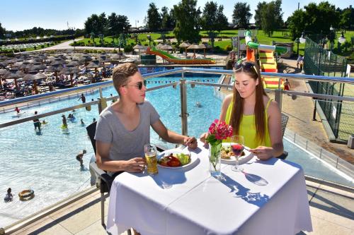 a man and a woman sitting at a table in front of a pool at Aquapark Health Resort & Medical SPA Panorama Morska All Inclusive in Jarosławiec