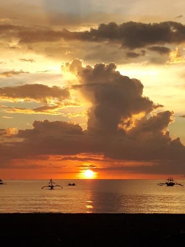 a sunset on the beach with a person holding a surfboard at Big BamBoo Beach Resort Sipalay in Sipalay