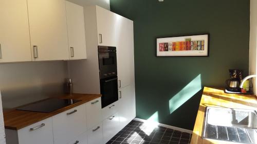 een keuken met witte kasten en een groene muur bij La petite maison in Aywaille