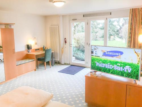 a living room with a flat screen tv and a desk at Hotel Birkenhof in Hanau am Main