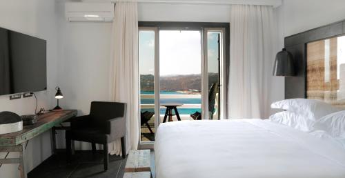 a bedroom with a bed and a desk and a window at Myconian Avaton, a Member of Design Hotels in Elia Beach