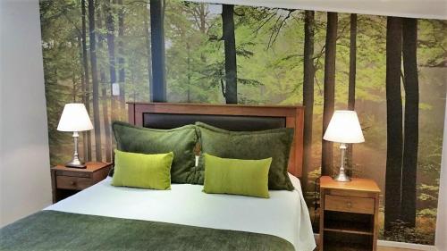a bedroom with a bed with two lamps and a forest mural at Hotel Puerta del Lago in Puerto Varas