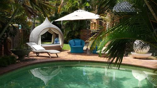 a patio area with a pool, chairs, and a umbrella at Ballina Palms Boutique Motel in Ballina