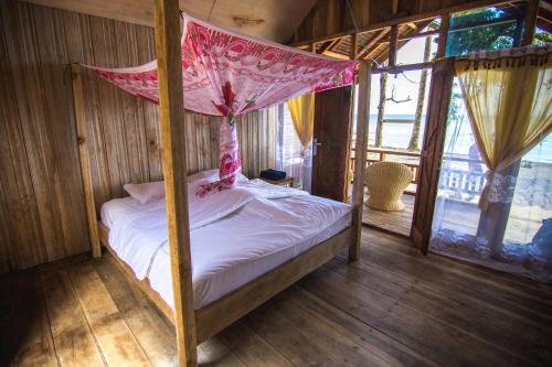 - une chambre avec un lit à baldaquin et des draps blancs dans l'établissement Pristine Paradise Dive Resort Una Una, à Pulau Unauna