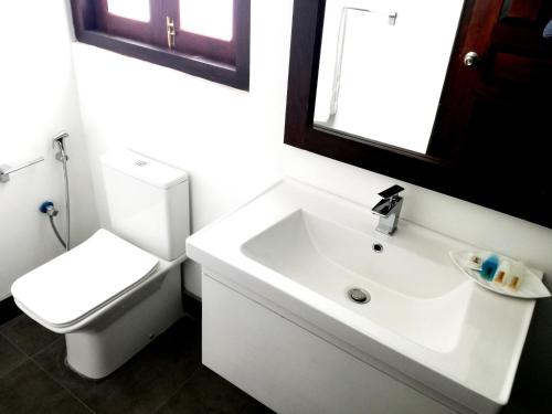 a white bathroom with a toilet and a sink at Hasara Hotel Galle in Galle
