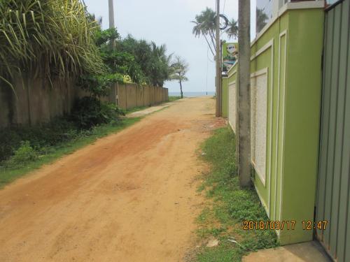 a dirt road next to a fence and the ocean at Larn's Villa Hotel & Apartment in Wadduwa