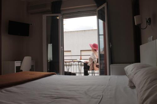 a woman in a pink hat looking out the window of a bedroom at Hotel Ramis fundado en 1969 in Ondara