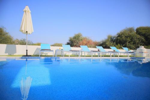 basen z niebiesko-białymi krzesłami i parasolem w obiekcie Akefalou Bay Villa w mieście Protaras