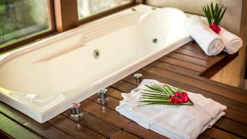 a bathroom with a tub and towels and a table with flowers at Sombra e Água Fresca Floresta in Pipa