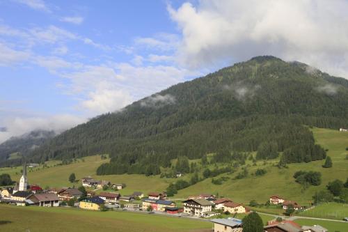 a village on a green hill with a mountain at Wohlfühlresort und Feriengut Martinerhof in Sankt Martin am Tennengebirge