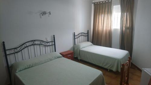 1 dormitorio con 2 camas y una ventana con cortinas en Hostal Tamarindos en Matalascañas