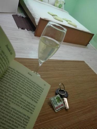 a glass of wine and a book and keys on a table at Apartman Andjela 1 in Vrdnik