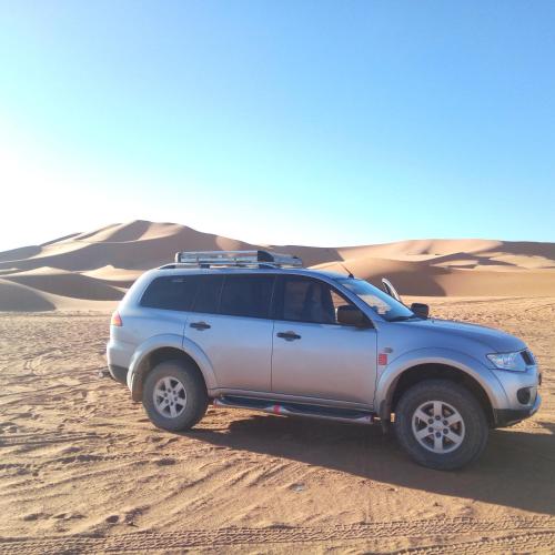 a suv parked in the sand in the desert at Sahara Desert Camp in Hassilabied