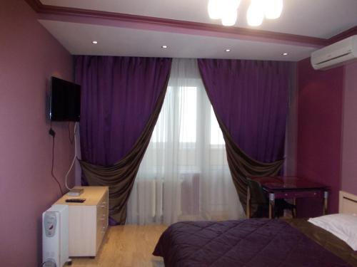 1 dormitorio con cortinas moradas, 1 cama y ventana en Alexandra Apartments, en Kiev