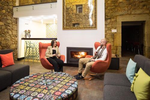 two people sitting in chairs in a living room with a fireplace at Cerca Design House in Fundão