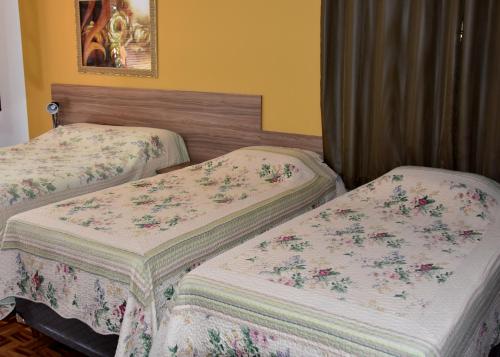 two beds in a hotel room with floral sheets at Hotel Cosini in São Sebastião do Paraíso