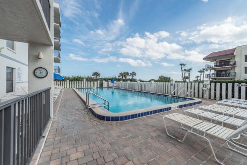 a swimming pool with chairs and a clock on a building at Cape Winds in Cape Canaveral